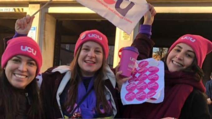Photo of left to right: Laura Loyola Hernandez, Vicky Blake, Dima Barakat Chami: three women all wearing winter coats and UCU pink beanie hats, with Vicky waving a UCU flag and Dima holding up a sheet of pink strike stickers